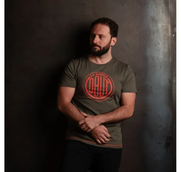 Camiseta Obut Caqui logo naranja Foto de un hombre con barba vistiendo una camiseta Obut Caqui con logo vintage naranja