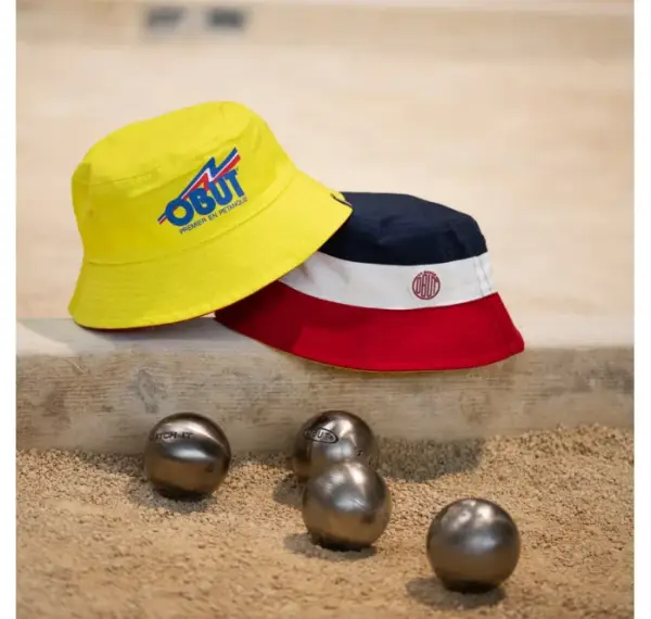 Gorro BOB Obut reversible amarillo/tricolor en una pista junto a bolas de petanca